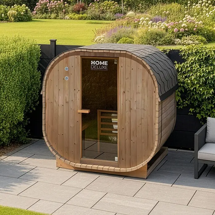Home Deluxe Fasssauna CUBE L - Elektroofen, Holz - Outdoor-Fasssauna aus hellem Holz mit dunklem Schindeldach, auf einer Terrasse.