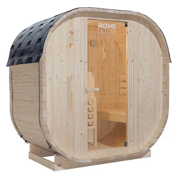 Home Deluxe Fasssauna CUBE M - Elektroofen, Holz - Eine helle Holzfasssauna mit dunklem Schindeldach und Glastür, mit Innenbank.
