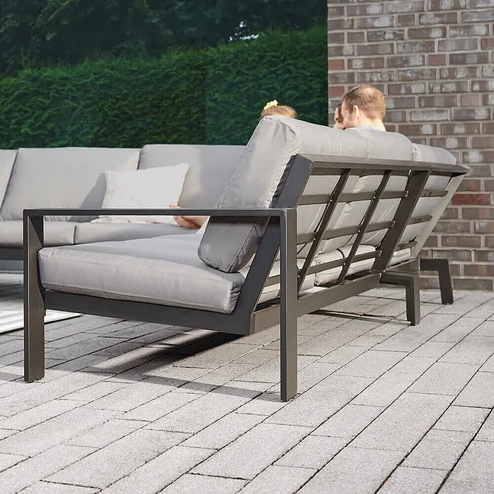 Home Deluxe Garten-Loungesessel RIO S -  - Dunkelgraues Metall-Gartensofa mit hellgrauen Polstern auf einer Terrasse, mit Personen.