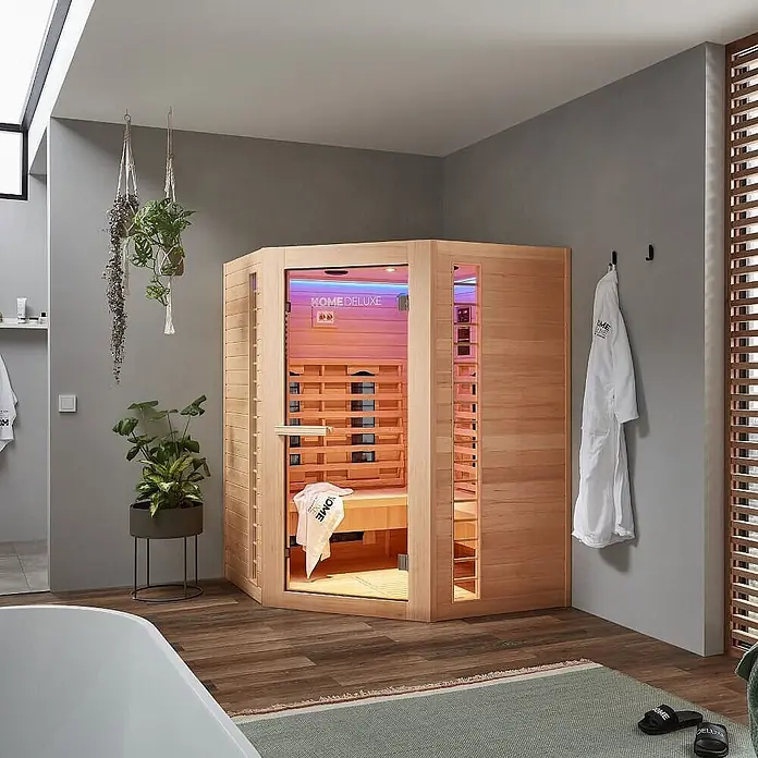 Home Deluxe Infrarotkabine REDSUN DELUXE XXL -  - Eck-Infrarotsaunakabine aus hellem Holz mit Glastür und farbiger Innenbeleuchtung, in einem modernen Wellnessbereich.