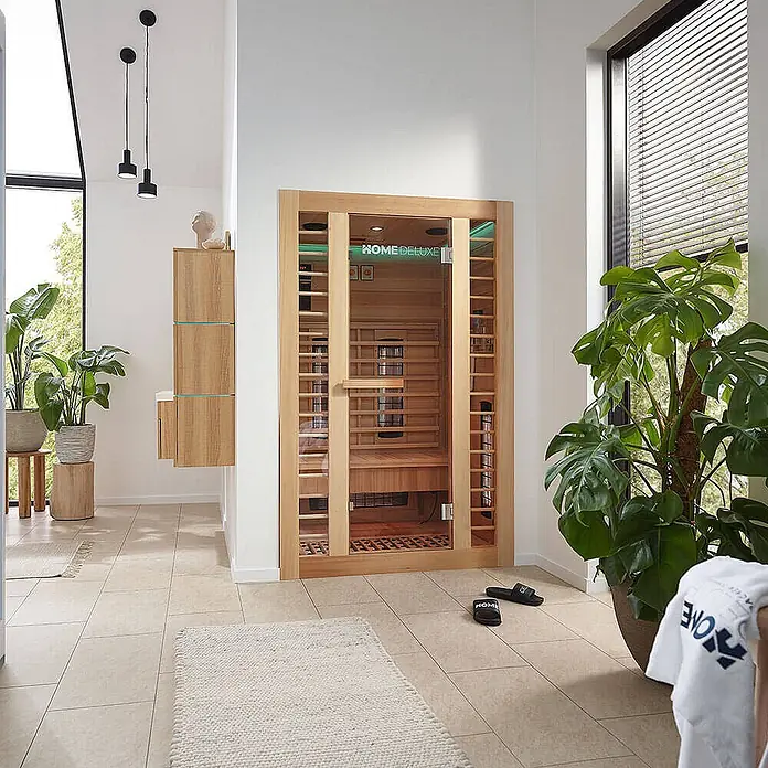 Home Deluxe Infrarotkabine REDSUM DELUXE PLUS M -  - Eine Infrarot-Saunakabine aus Holz mit Glastür, innen mit Holzbank und Heizstrahlern, in einem modernen Wellnessbereich zu Hause.