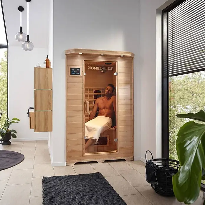 Home Deluxe Infrarotkabine REDSUN M -  - Mann entspannt sich in einer hellen HOME DELUXE Infrarotsauna aus Holz in einem modernen Raum.