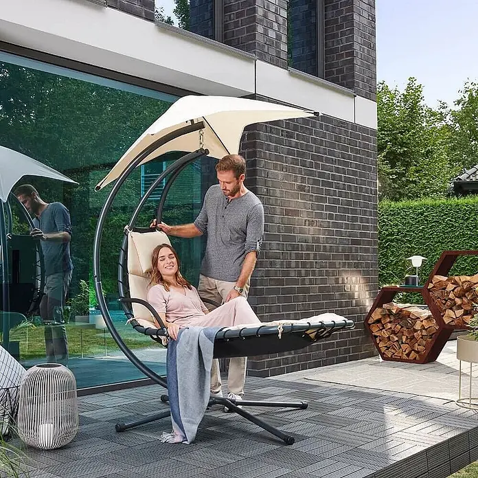 Home Deluxe Gartenliege SAN REMO - Anthrazit / Beige, Polyester - Ein Paar entspannt sich auf einem schwarzen Hängeliegestuhl mit beigen Kissen und Sonnendach.