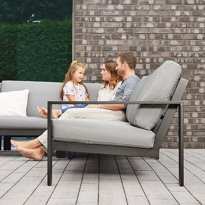 Home Deluxe Garten-Loungesessel RIO S -  - Graues Outdoor-Lounge-Set mit dunkelanthrazitfarbenem Metallrahmen, auf dem eine Familie bequem auf einer gepflasterten Terrasse sitzt.