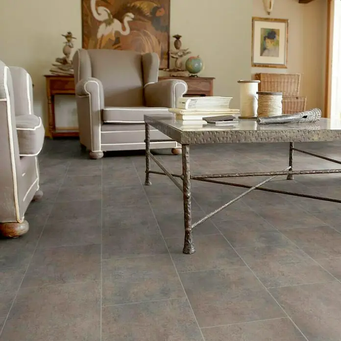 Tarkett Suelo de PVC a metros Matrix Melbourne - Efecto de baldosa, Marrón, Ancho: 3 m - Una sala de estar con muebles elegantes y un pavimento elegante que añade calidez a la habitación. Las baldosas del suelo son rectangulares y gris-marrón.