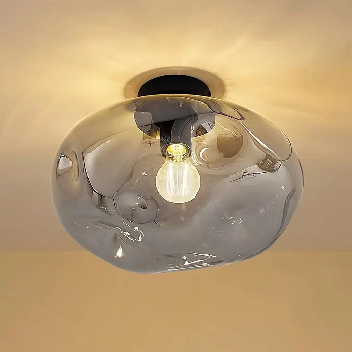 Lindby Deckenleuchte Lelia - alu / grau / zink, E27 - Deckenleuchte mit unregelmäßigem rauchgrauem Glasschirm und sichtbarer Glühbirne, auf schwarzem Sockel montiert.
