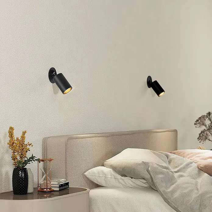 Arcchio Einbauleuchte Davin - schwarz, schwarz - Zwei schwarze zylindrische Wandstrahler über einem Bett in einem hellen Schlafzimmer, die akzentuierte Beleuchtung spenden.