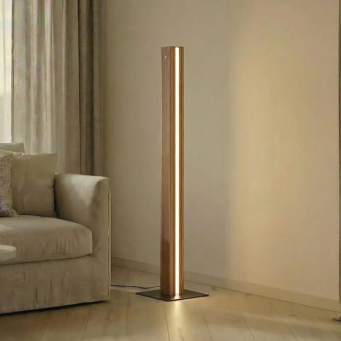 Lucande Stehleuchte Lieske - Höhe: 122 cm, schwarz, Holz hell - Eine moderne, hohe Holz-Stehleuchte mit integriertem LED-Lichtband steht neben einem beigen Sofa auf Holzboden und beleuchtet den Raum warm.