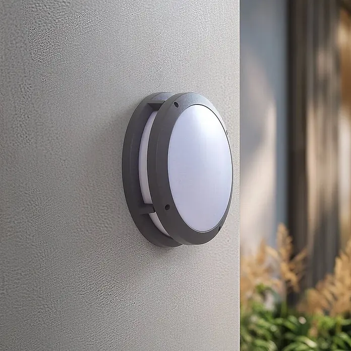 Lindby Außenwandleuchte Liren - alu / grau / zink, IP54 - Runde, dunkelgraue Außenwandleuchte mit weißem Diffusor, an einer strukturierten Wand montiert.