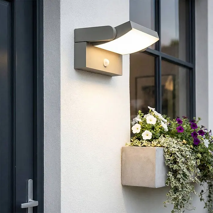 Lindby Außenwandleuchte Sherin - alu / grau / zink, IP54 - Graue verstellbare Außenwandleuchte mit integriertem Bewegungsmelder, beleuchtet eine Außenwand.