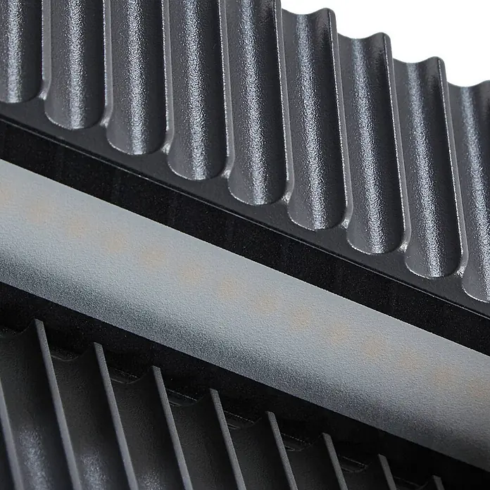 Lucande Außenwandleuchte Tavion - schwarz, schwarz, IP65 - Nahaufnahme einer dunkelgrauen LED-Leuchte aus Metall mit Kühlrippen und mattiertem LED-Streifen mit sichtbaren LEDs.