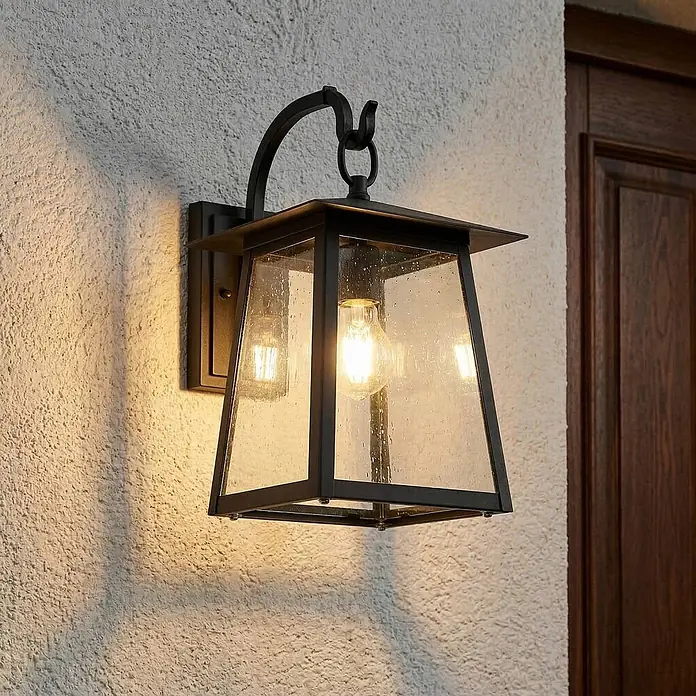 Lucande Außenwandleuchte Xavon - 28,2 x 24 x 38 cm, schwarz, schwarz, IP44 - Schwarze Outdoor-Wandleuchte aus Metall mit strukturiertem Glas und leuchtender Glühbirne an einer texturierten Wand.