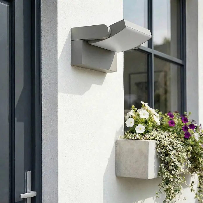 Lindby Außenwandleuchte Sherin - alu / grau / zink, IP54 - Moderne graue Außenwandleuchte an einer weißen Putzfassade über einem Blumenkasten.