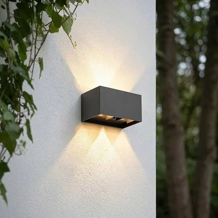 Lindby Außenwandleuchte Nivar - 10 x 20 x 10 cm, schwarz, schwarz, IP54 - Dunkelgraue rechteckige Außenwandleuchte an einer strukturierten Wand, die warmes Licht nach oben und unten abgibt.