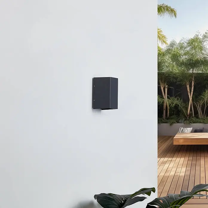 Lucande Außenwandleuchte Kimian - schwarz, schwarz, IP54 - Dunkelgraue, rechteckige Außenwandleuchte an einer weißen Wand, die einen Gartenbereich beleuchtet.