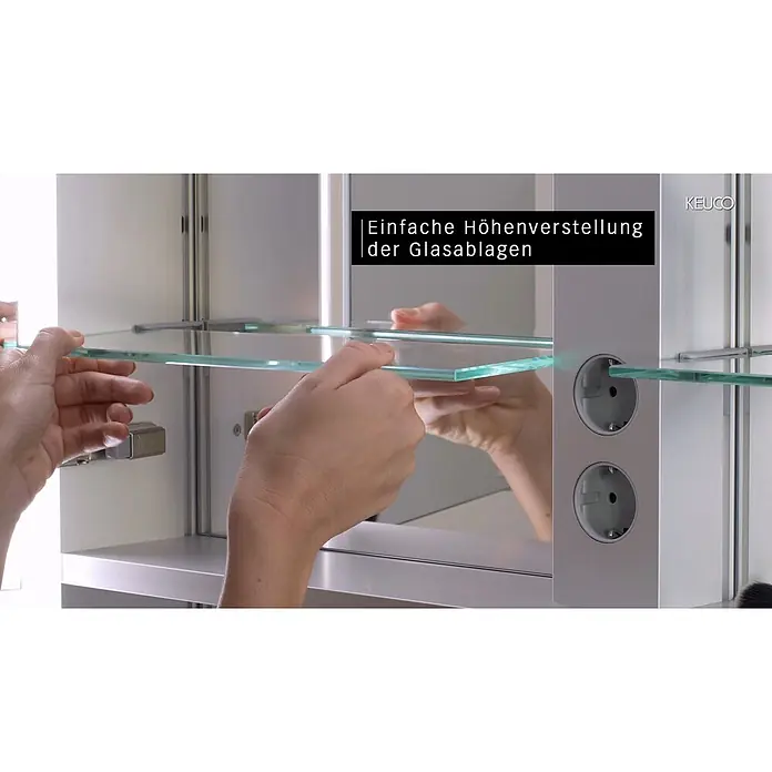 Keuco LED-Spiegelschrank Royal Lumos - B x H: 120 x 73,5 cm, Aluminium, silber-eloxiert - Hände verstellen eine klare Glasablage in einem silbernen Spiegelschrank mit integrierten Steckdosen.