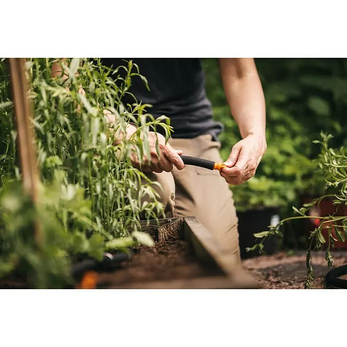 Fiskars Tropfschlauch - 15 m - Detailaufnahme einer Person, die einen Bewässerungsschlauch im Garten vorbereitet, um Pflanzen zu bewässern.\n