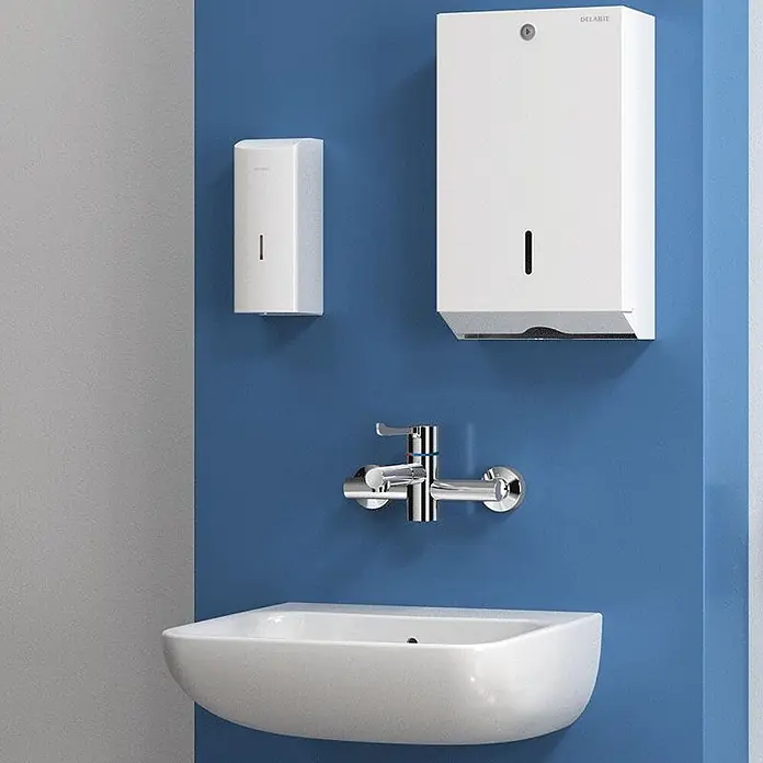 Delabie Spültischarmatur Delabie -  - Weiße wandmontierte Spender (Seife, Papier) über einem weißen Waschbecken mit Chromarmatur an einer blauen Wand.