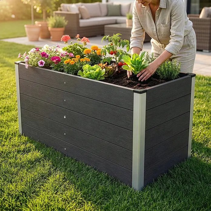 Floordirekt Hochbeet Delos - 150 x 70 x 75 cm, WPC, Anthrazit - Dunkelgraues Hochbeet aus WPC mit Aluminiumecken, bepflanzt mit Blumen und Gemüse, wird von einer Person im Garten gepflegt.