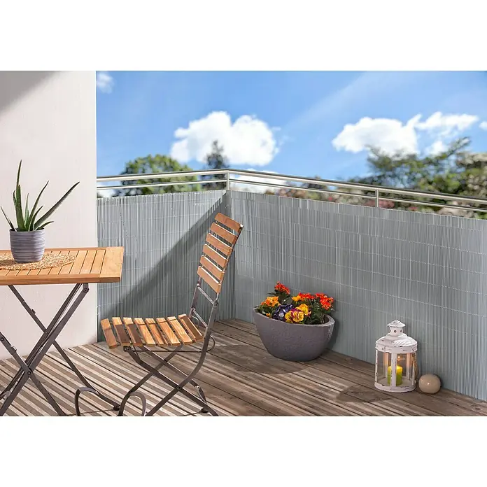 Sichtschutzmatte - 300 x 90 cm, Kunststoff, Silber - Eine stilvolle Outdoor-Szene mit einem Holztisch, Stuhl, Pflanzen und einer grauen Sichtschutzwand auf einem Balkon.