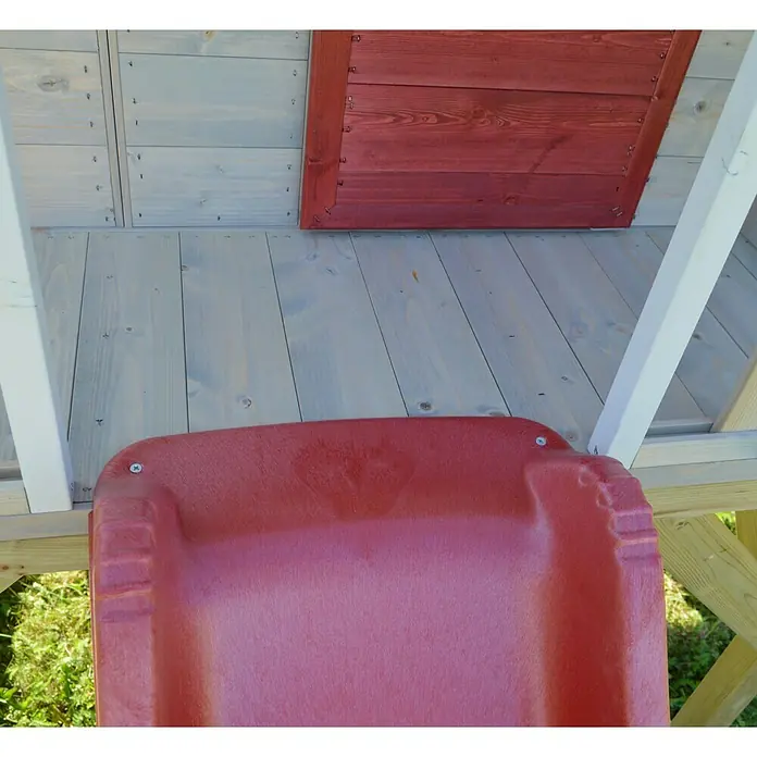 Wendi Toys Spielhaus Alpaka - Glas, Natur/Rot - Nahaufnahme einer roten Kinderrutsche, die an einem Spielhaus aus Holz befestigt ist, mit Blick auf das grüne Gras im Hintergrund.