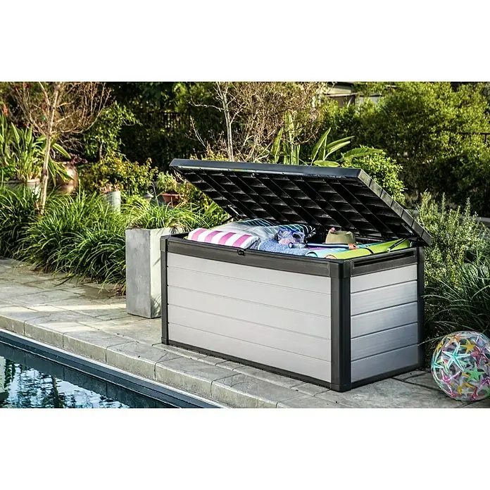 Keter Gartenbox Denali - 151,7 x 72,5 x 70 cm, Kunststoff - Eine graue Gartenbox mit geöffnetem Deckel, gefüllt mit Strandtüchern und Spielsachen, steht neben einem Pool.