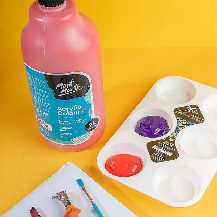 Mont Marte Acrylfarbe Signature - Brillantrot, 2.000 ml, Flasche mit Tropfpipette - Große rosa Flasche Mont Marte Brillantrot Acrylfarbe, weiße Palette mit roter und lila Farbe, Pinsel auf gelbem Untergrund.