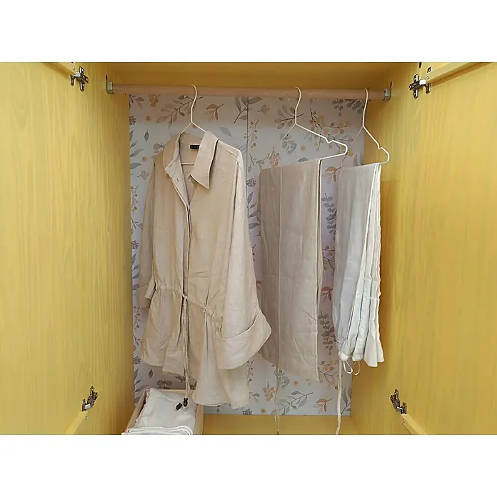 Astigarraga Vita Armario para ropa - L x An x Al: 48 x 80 x 180 cm, Natural - Abrigo y pantalones de lino beige colgando en un armario de madera amarillo con papel pintado floral.