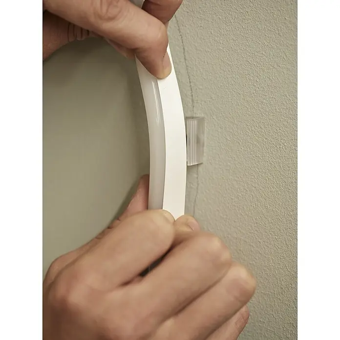 Ledvance LED-Band Outdoor Neon Flex Digital - Länge: 3 m, Lichtfarbe: RGBW, 15 W, 120 lm - Hände installieren einen weißen flexiblen LED-Streifen in eine transparente Montageklammer an einer strukturierten Wand.