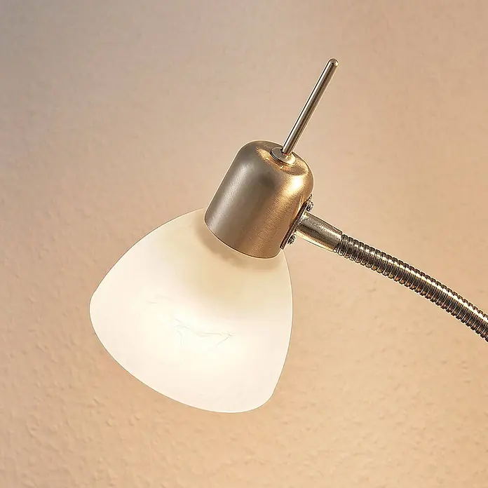 Lindby Stehleuchte Gwendolin - Höhe: 160 cm, alu / grau / zink, E14 - Nahaufnahme eines beleuchteten Lampenkopfs mit weißem Marmorglas-Schirm und gebürstetem Messinggestell an flexiblem Arm.