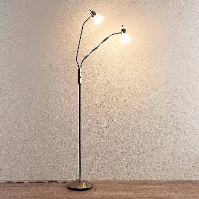 Lindby Stehleuchte Gwendolin - Höhe: 160 cm, alu / grau / zink, E14 - Zweiflammige Stehleuchte mit Chrom-Finish und weißen Schirmen auf Holzfußboden vor heller Wand.