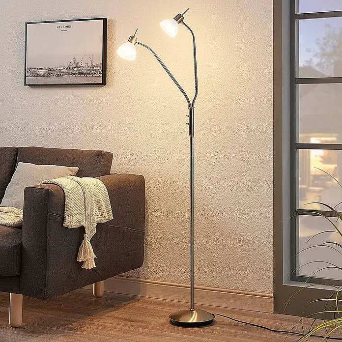 Lindby Stehleuchte Gwendolin - Höhe: 160 cm, alu / grau / zink, E14 - Stehleuchte aus gebürstetem Nickel mit zwei flexiblen Armen und weißen Glasschirmen, spendet Licht neben einem braunen Sofa.