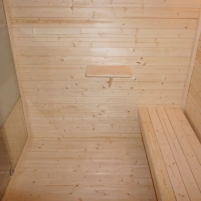 Home Deluxe Fasssauna TALO XL - Elektroofen, Holz - Sauna-Innenraum mit hellen Holzvertäfelungen an Wänden und Boden, einer Bank und einem kleinen Regal.