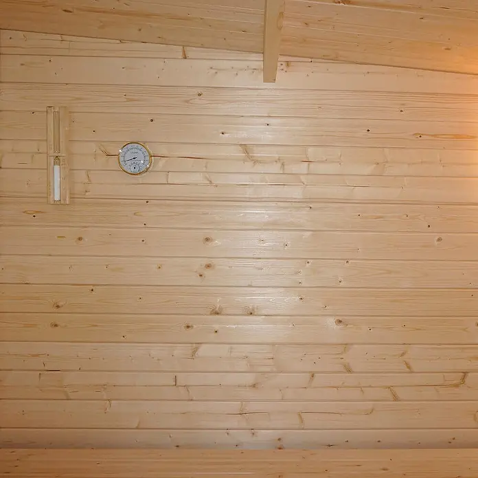 Home Deluxe Fasssauna TALO XL - Elektroofen, Holz - Heller Saunainnenraum aus Holz mit Thermometer und Sanduhr an der Wand.