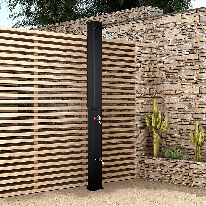 Home Deluxe Solardusche OLYMP - Kunststoff, Schwarz Matt, 40 l - Schwarze Außendusche mit Kopfbrause, Handbrause und Fußhahn, neben einem Holzlamellen-Sichtschutz installiert.