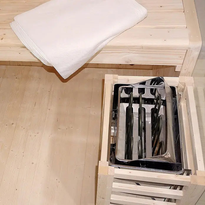 Home Deluxe Elementsauna SHADOW BIG XL - Elektroofen, Steuerung Ofen: Integriert, L x B x H: 200 x 200 x 190 cm - Saunaofen aus Edelstahl in einer Holzkiste neben weißen Saunatextilien auf einer Holzbank.