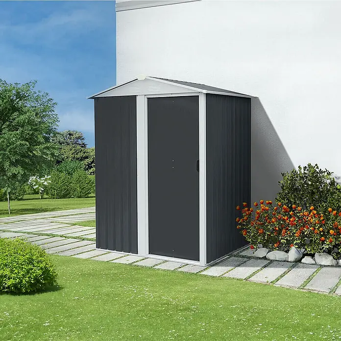 Home Deluxe Gerätehaus BOHIO S (B x L x H) 151 x 110 x 189 cm - Außenbreite inkl. Dachüberstand: 151 cm, Außentiefe inkl. Dachüberstand: 110 cm, Stahl, Anthrazit - Dunkelgraues Metall-Gartenhaus mit weißem Rahmen, an einer Hauswand im Garten.