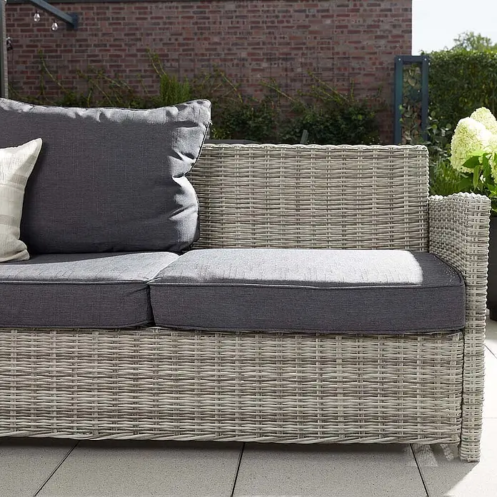 Home Deluxe Polyrattan Sitzgruppe BAHIA Mit Regenabdeckung -  - Helles graues Rattan-Outdoor-Sofa-Element mit dunkelgrauen Kissen auf einer Terrasse.