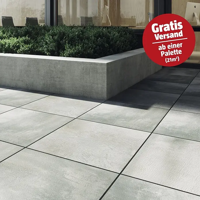 Cersanit Terrassenfliese Beton Grey Light - 59,3 x 59,3 x 2 cm, Grau, Matt - Hellgraue Outdoor-Fliesen auf einer Terrasse, neben einem Betonkübel mit grünen Büschen.