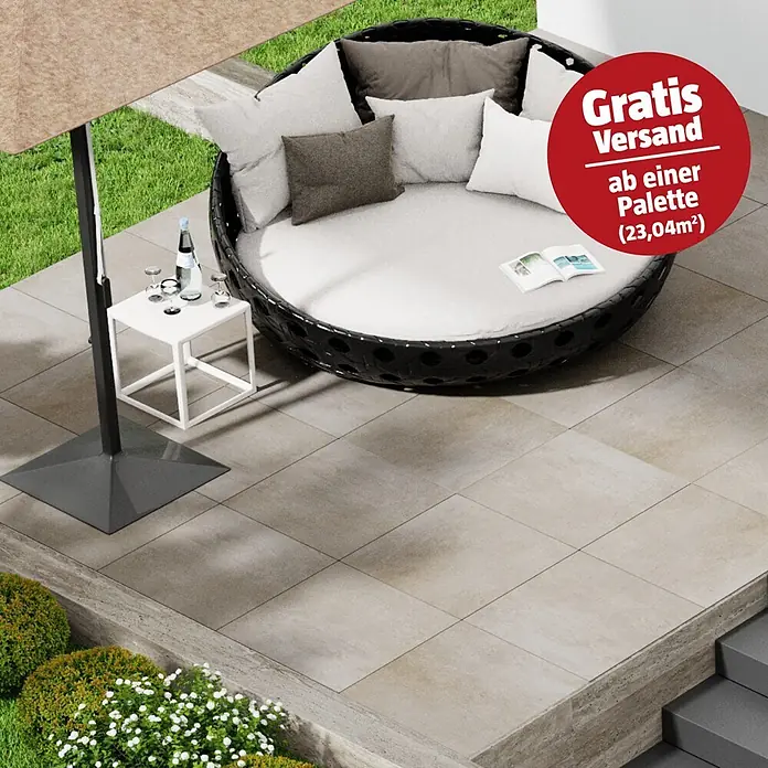 Marazzi Terrassenfliese Esterno 20T Plaster Sand - 60 x 60 x 2 cm, Sand, Matt - Rundes Lounge-Bett aus dunklem Rattan mit hellen Kissen, Sonnenschirm und Beistelltisch auf beigefarbener Fliesenterrasse.