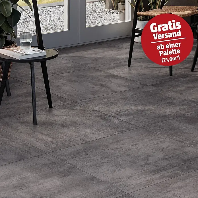 Atlas Concorde Solution Terrassenfliese Rover Smoke - 60 x 60 x 2 cm, Anthrazit, Matt - Dunkelgraue Bodenfliesen in einem modernen Wohnbereich mit Tischen und Stühlen, mit subtilen Texturvariationen.