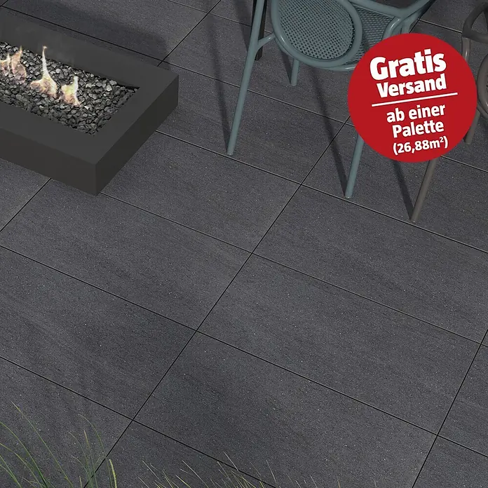 Terrassenfliese Kamari 2.0 - 39,7 x 79,7 x 2 cm, Anthrazit, Matt - Dunkelgraue Terrassenplatten mit feiner Textur, im Außenbereich mit Feuerstelle und Stühlen verlegt.