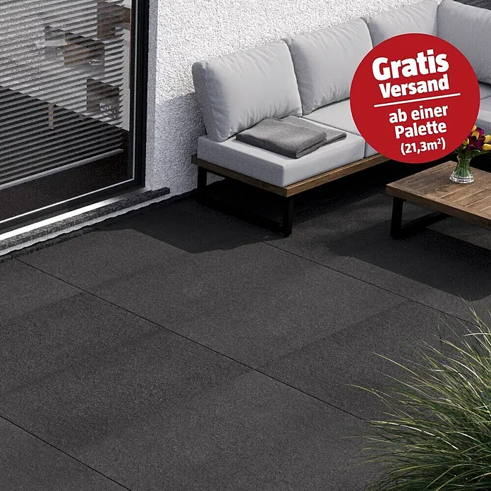 Terrassenfliese Basalt 2.0 - 59,7 x 119,7 x 2 cm, Basaltgrau, Matt - Dunkelgraue, großformatige Terrassenplatten. Gezeigt in einer modernen Terrassenumgebung mit Sofa und Couchtisch.