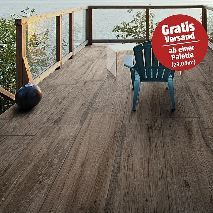 Terrassenfliese Essenze 2.0 - 40 x 120 x 2 cm, Musk, Matt - Brauner Fliesenboden in Holzoptik auf einer Außenterrasse mit Blick auf Wasser, Stuhl und Tisch.