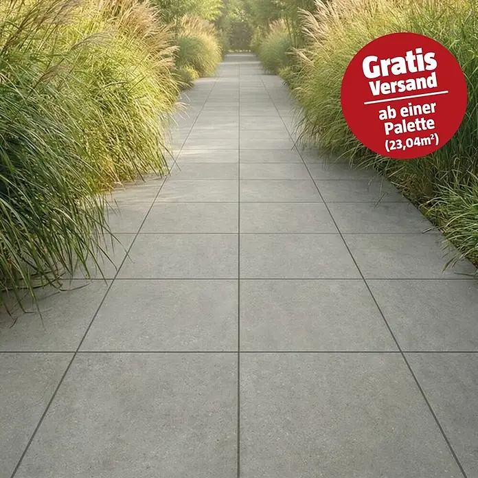 Terrassenfliese Portland - 60 x 60 x 2 cm, Londra, Matt - Graue Terrassenplatten bilden einen Gartenweg, gesäumt von hohem grünem Ziergras, mit rotem Kreis 'Gratis Versand!'.