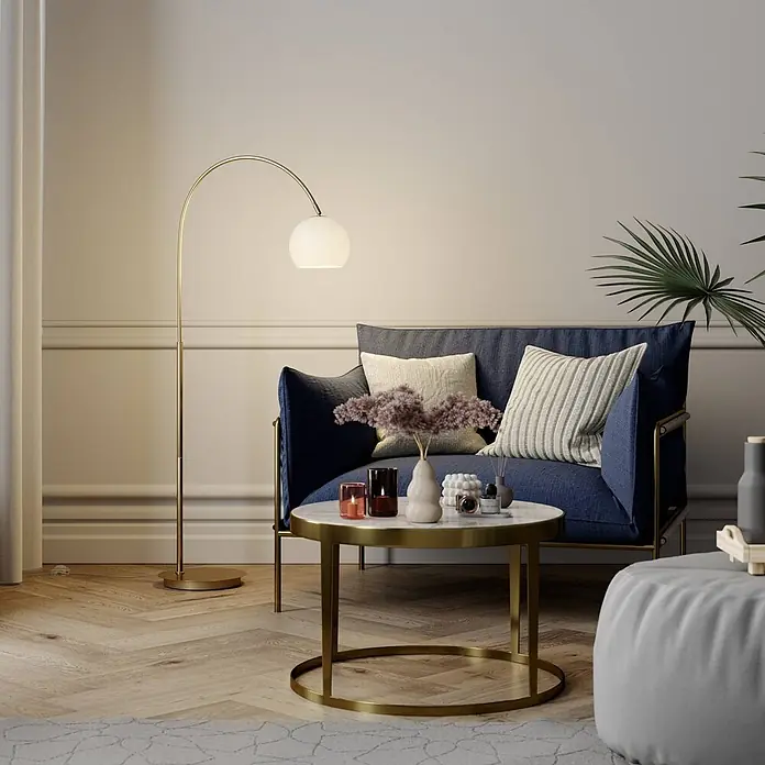 Lindby Stehleuchte Cynthia - Höhe: 140 cm, messing / gold, E27 - Goldene Bogenstehlampe mit weißem Kugelschirm, spendet warmes Licht neben einem blauen Sessel.