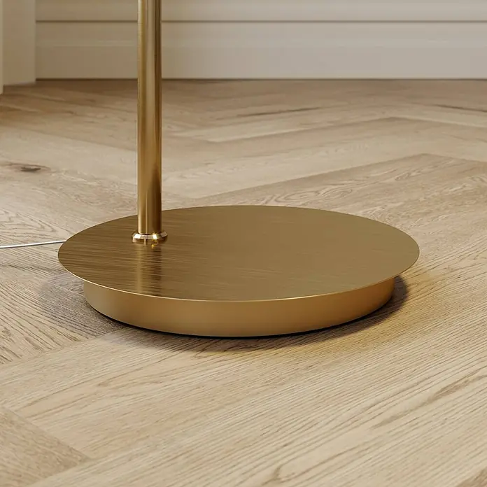 Lindby Stehleuchte Cynthia - Höhe: 140 cm, messing / gold, E27 - Runder, gebürsteter Messing-Stehlampenfuß mit Stange und weißem Kabel auf hellem Holzfußboden.
