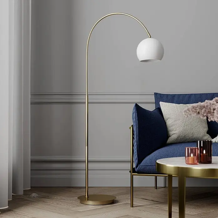 Lindby Stehleuchte Cynthia - Höhe: 140 cm, messing / gold, E27 - Goldene Bogenstehlampe mit weißem Kugelschirm, beleuchtet eine Wohnzimmerkulisse neben einem blauen Sofa.