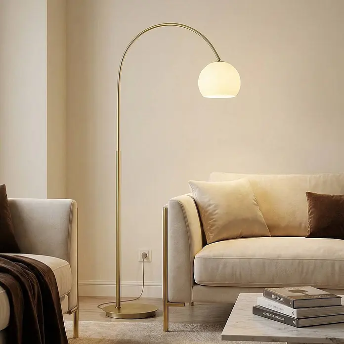 Lindby Stehleuchte Cynthia - Höhe: 140 cm, messing / gold, E27 - Goldene Bogen-Stehlampe mit kugelförmigem weißem Glasschirm, neben einem beigen Sofa in einem modernen Wohnzimmer.