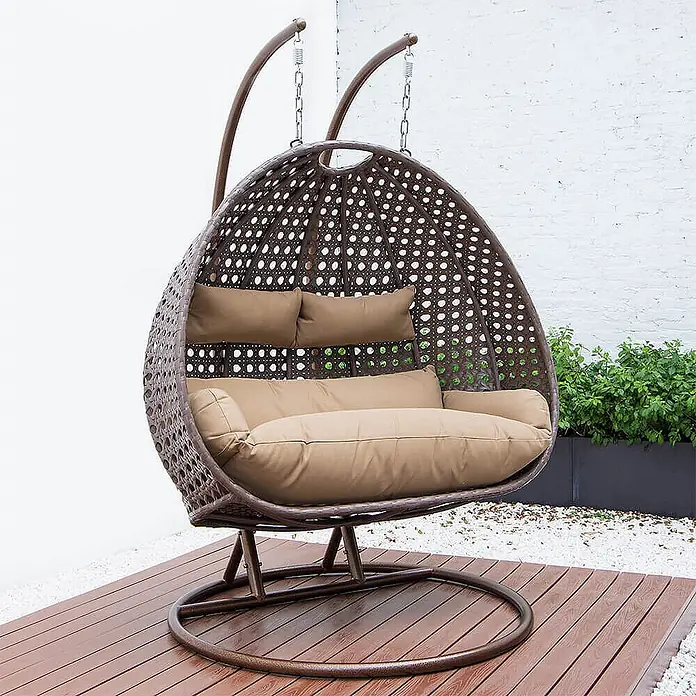 Home Deluxe Hängesessel TWIN - Kunststoff, Braun - Brauner Hängesessel im Rattan-Stil mit beigen Kissen auf einer Holzterrasse.
